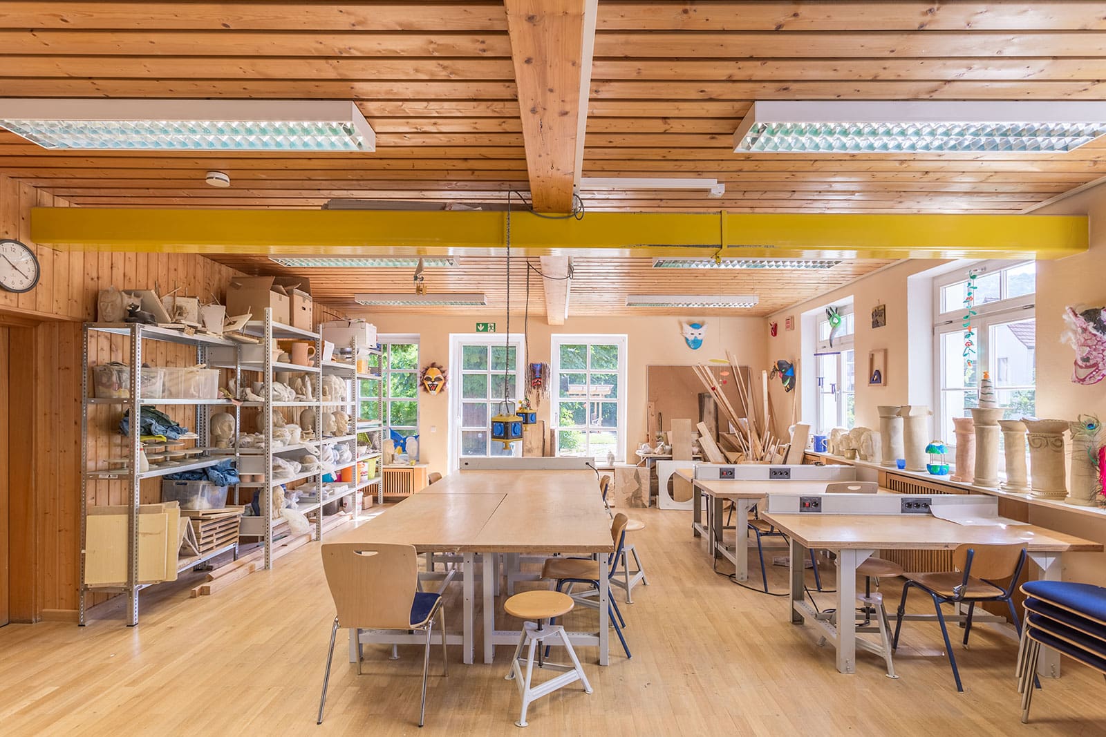 Großer Werk- und Kreativraum mit Holztischen, Regalen, Bastelmaterial und Holzdecke.