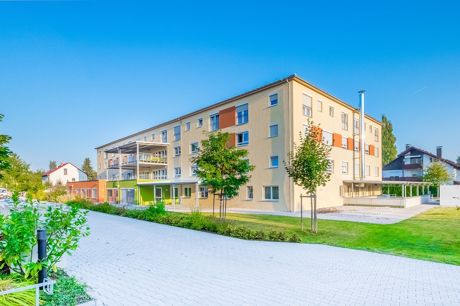 Außenansicht eines modernen mehrstöckigen Gebäudes mit Balkonen, Grünflächen und gepflastertem Weg.
