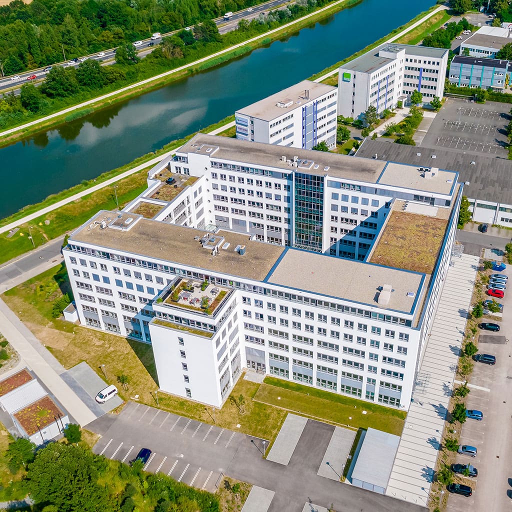 Luftaufnahme eines großen Gebäudekomplexes mit Parkplätzen und Grünflächen.