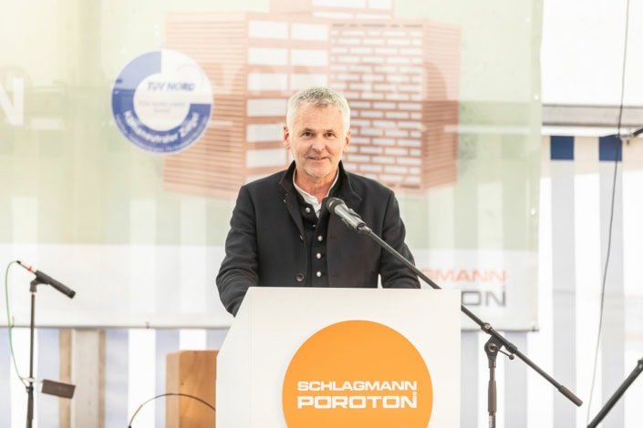 Redner steht an einem Podium vor Publikum und Backsteinwand
