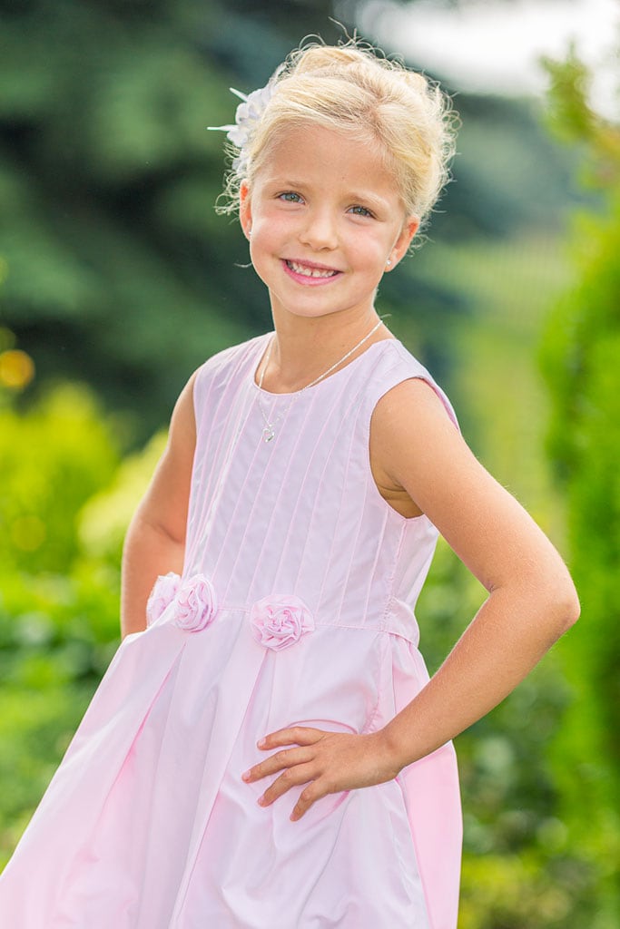Kindergartenmädchen im rosa Sommerkleid stellt sich für Kindergartenfotos in Positur.