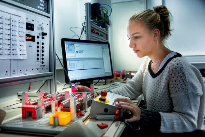 Mitarbeiterin arbeitet an einem technischen Arbeitsplatz mit Monitor und Steuergerät