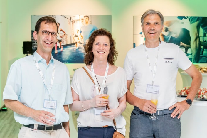 Drei Aussteller lächeln an einem Messestand in heller Umgebung