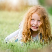 Im Gras liegendes rothaarige kleines Mädchen lässt sich im Kindergarten fotografieren.