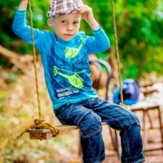 Junge mit Mütze und blauer Kleidung sitzt auf der Schaukel. Moderne und kreative Kindergartenfotografi in Fürth, Nürnberg und im Umland
