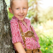 Fotoshooting im Kindergarten mit einem Jungen, der eine bayerische Tracht trägt und an einem Baum lehnt.