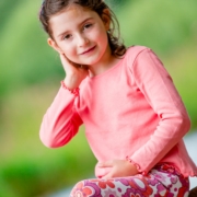 Sitzendes, rosa gekleidetes, dunkelhaariges Mädchen schaut in die Kamera des Kindergartenfotografen.