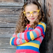 Kindergartenkind mit gelber Brille und bunten Pullover lehnt am Zaun