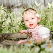 Süßes Kinderfoto, im Kinderhort aufgenommen. Lachendes Baby sitzt mit Blumenkranz im Haar in der Wiese