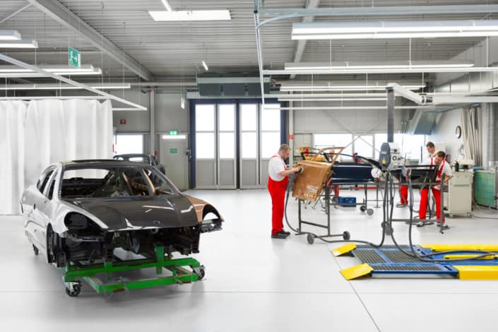 Industriehalle mit Fahrzeugkarosserie und Mitarbeitenden im Arbeitsbereich
