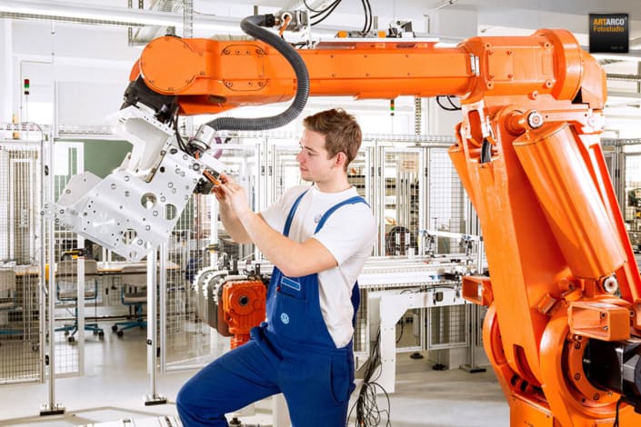 Mitarbeiter arbeitet in einer Industriehalle an einer Anlage mit Roboterarm