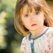 Portrait, Foto eines blonden Mädchen im Kindergartenalter. Es trägt ein weiß/blaues Kleid und schaut direkt in die Kamera des Kindergartenfotografen