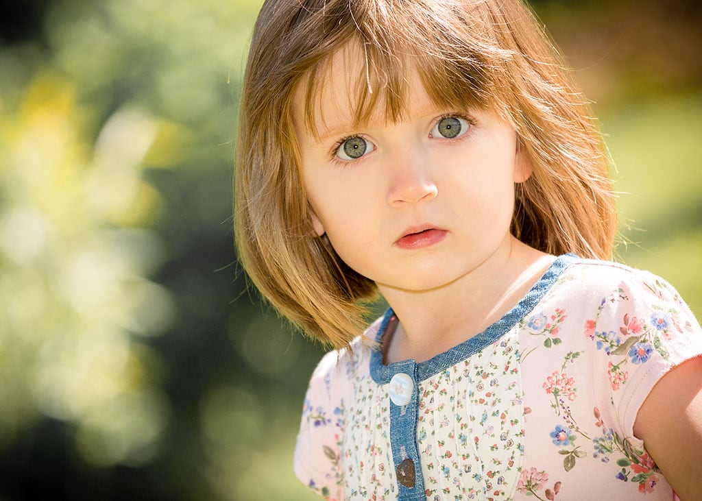 Portrait, Foto eines blonden Mädchen im Kindergartenalter. Es trägt ein weiß/blaues Kleid und schaut direkt in die Kamera des Kindergartenfotografen