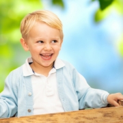 Blondhaariger Junge sitzt in einer Holzkiste im Kindergarten, bereit für coole Kindergartenfotos.