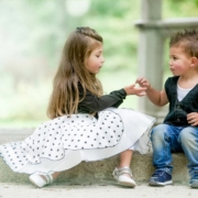 Kindergartenfotografie einmal anders. Schick angezogenes Geschwisterpaar sitzt im Kindergarten auf einer Steinmauer und wird fotografiert.