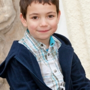 Kinderfoto. Ein Junge mit blauem Hemd und Jacke schmunzelt freundlich in Richtung der Fotokamera. Moderne und kreative Kindergartenfotografie in Fürth, Nürnberg und im Umland