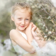 Niedliches Kindergartenfoto, leicht entsättigt. Lächelndes Kind im weißen Kleid sitzt im Blumenmeer.